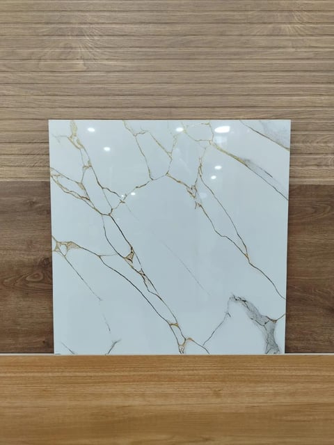 White marble tile with gold and gray veining displayed on a wooden surface