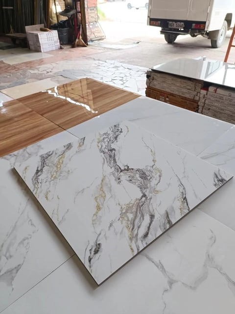 Marble-look tile samples displayed on outdoor warehouse floor with wood flooring and truck in background