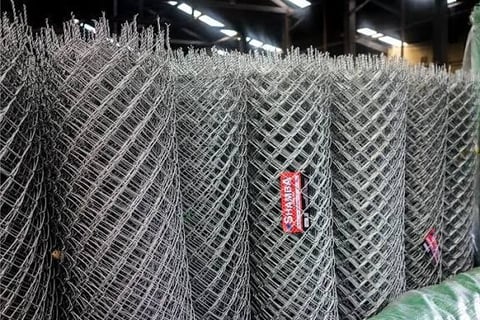 Rolls of galvanized chain-link fencing stacked in an industrial warehouse with overhead lighting