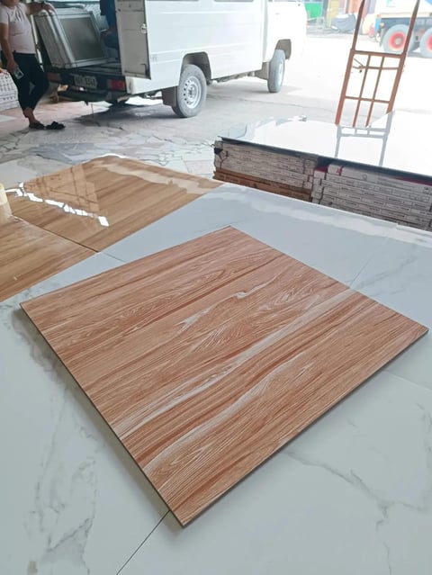 Wood grain ceramic tiles displayed on white floor with delivery truck and materials in background