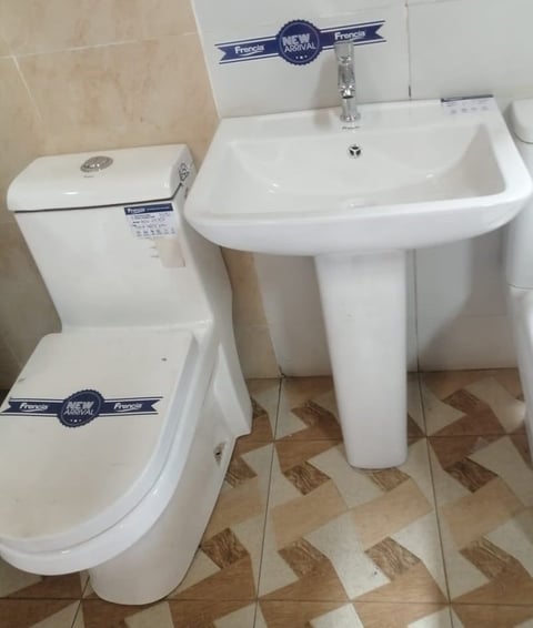 Modern bathroom fixtures including a white pedestal sink, matching white toilet with seat, and tiled floor with geometric brown pattern