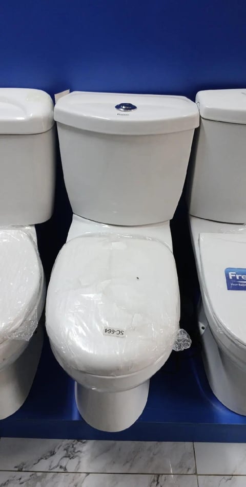 Two-piece white toilet with closed lid displayed on blue platform at showroom, with matching fixtures visible on sides
