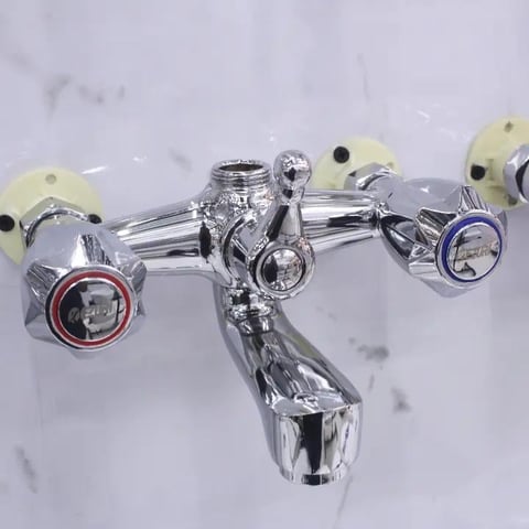 Overhead view of a polished chrome bathroom faucet with dual handles, gauges, and cream-colored valve caps on a marble surface