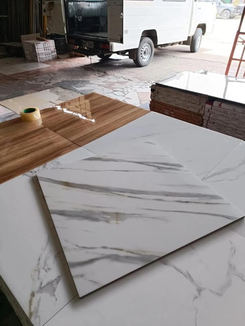 Marble and wood flooring samples displayed on white surface in showroom with vehicle and storage in background