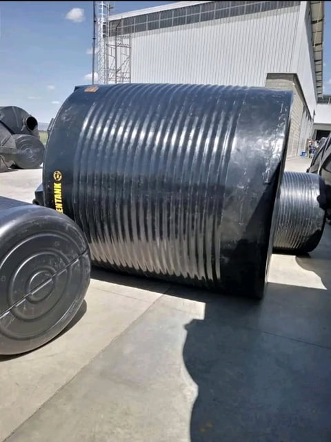 Large corrugated metal storage tank or industrial equipment with vertical ribbing on concrete surface at industrial facility