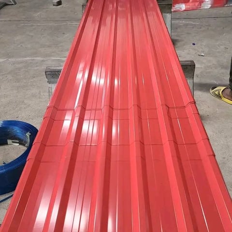 Red corrugated metal roofing sheets laid out on concrete floor in warehouse