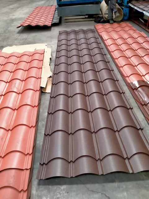 Corrugated metal roof tiles in red and brown colors arranged on a concrete floor at an industrial facility