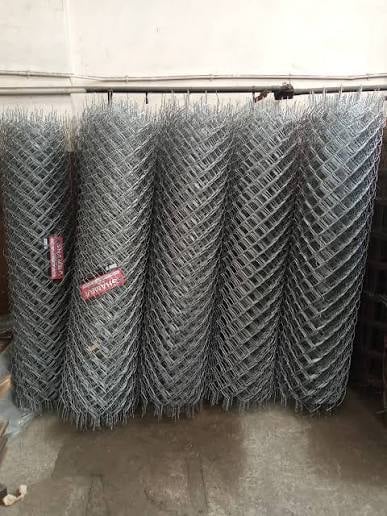 Rolls of galvanized diamond-pattern chain-link fencing hung on a horizontal bar in a storage area