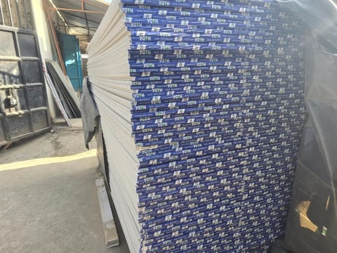 Stack of white and blue labeled insulation boards leaning against a building wall in an industrial storage area
