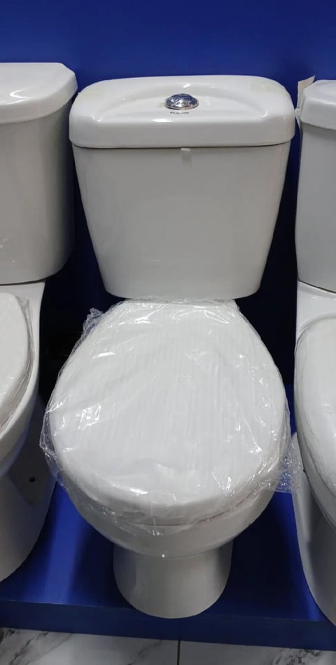 White ceramic two-piece toilet with plastic wrap on seat and tank, displayed against blue background in showroom