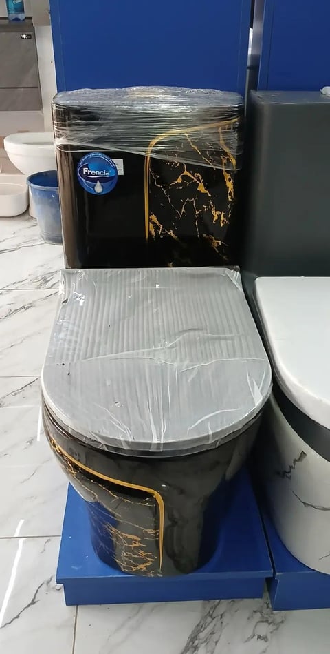 Black toilet with gold marbling and plastic wrapping on seat, displayed in showroom with blue backdrop