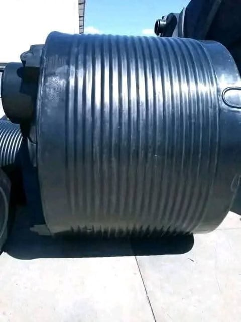 Large cylindrical metal drum or container with deep ridged grooves, mounted on industrial equipment outdoors against a clear blue sky