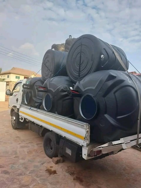 Pickup truck loaded with large black plastic water storage tanks in an outdoor residential area