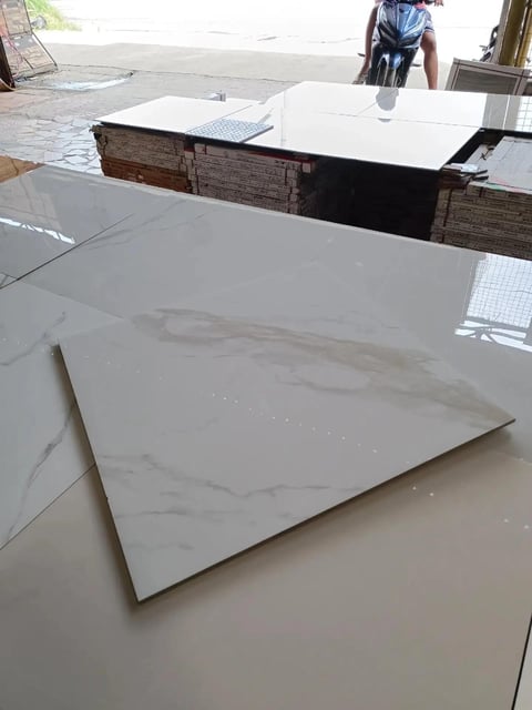 White marble tile samples displayed on floor with additional tiles on counter in showroom or warehouse