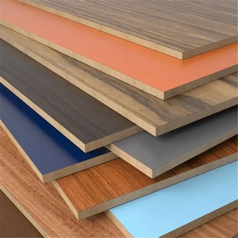 Stacked laminate flooring samples showing various colors including wood, gray, black, blue, coral, and light blue finishes