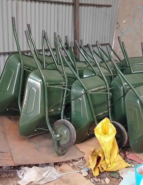 Row of green wheelbarrows with metal handles stacked upright in a warehouse, with yellow protective covering visible