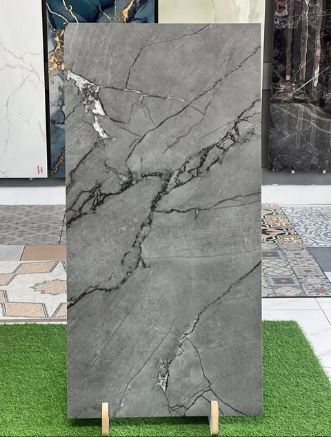 Gray marble tile sample with black veining displayed vertically with other flooring and design samples in background