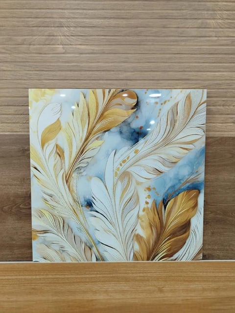 Abstract watercolor painting with gold and blue feather designs on white background displayed on wooden surface