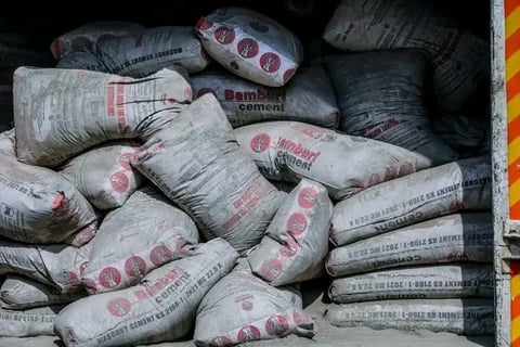 Stacked bags of cement with red circular logos in an orange-edged container, ready for construction use