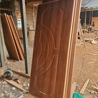 Dark wooden door with ornate carved spiral design leaning against workshop wall with construction materials