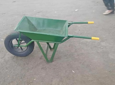 Green single-wheeled wheelbarrow with metal frame and yellow handles on concrete ground