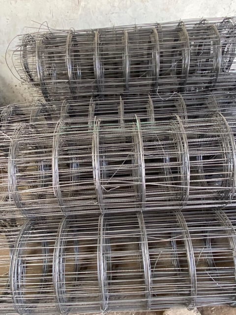 Rolls of welded wire mesh fencing material stacked and stored on ground