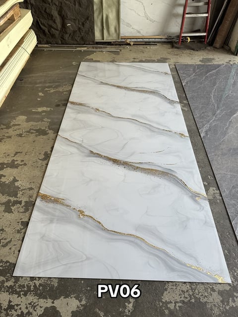 White and gray marble tile sample with gold veining displayed on concrete floor, labeled PV06