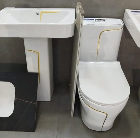 White bathroom fixtures with gold trim including a pedestal sink and toilet displayed in a showroom
