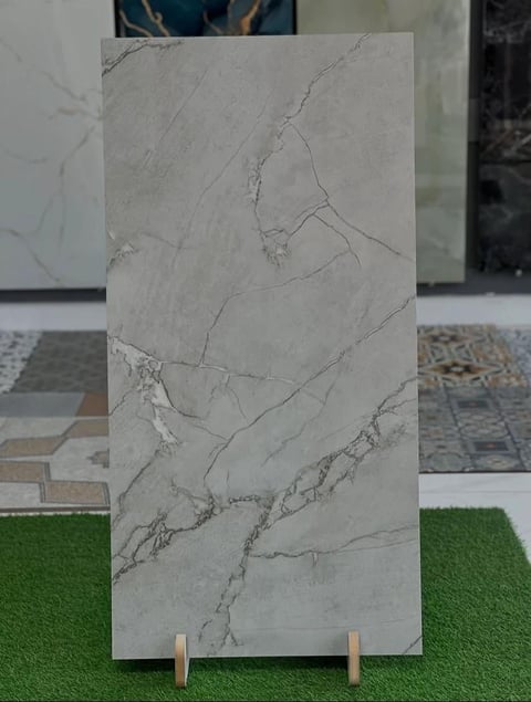 Light gray marble tile sample with natural veining displayed on wooden easel in showroom setting