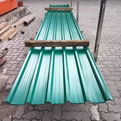 Two sheets of green corrugated metal roofing panels stacked on a paved outdoor surface