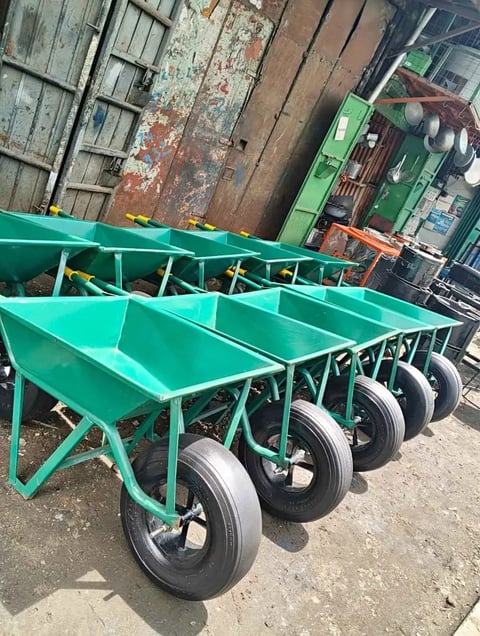 Row of green wheelbarrows with metal frames and large wheels parked in a line at a construction or agricultural supply yard
