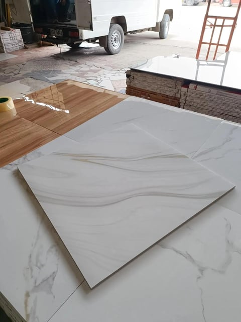 White marble-pattern ceramic tile displayed on flooring samples in a showroom with construction materials visible in background