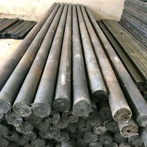 Stack of gray metal cylindrical pipes arranged in rows on a concrete surface