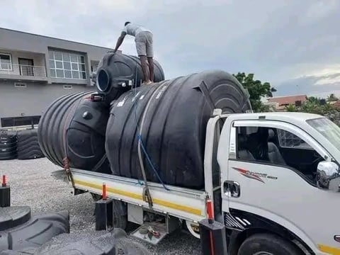 White truck loaded with large black cylindrical water tanks on a construction site