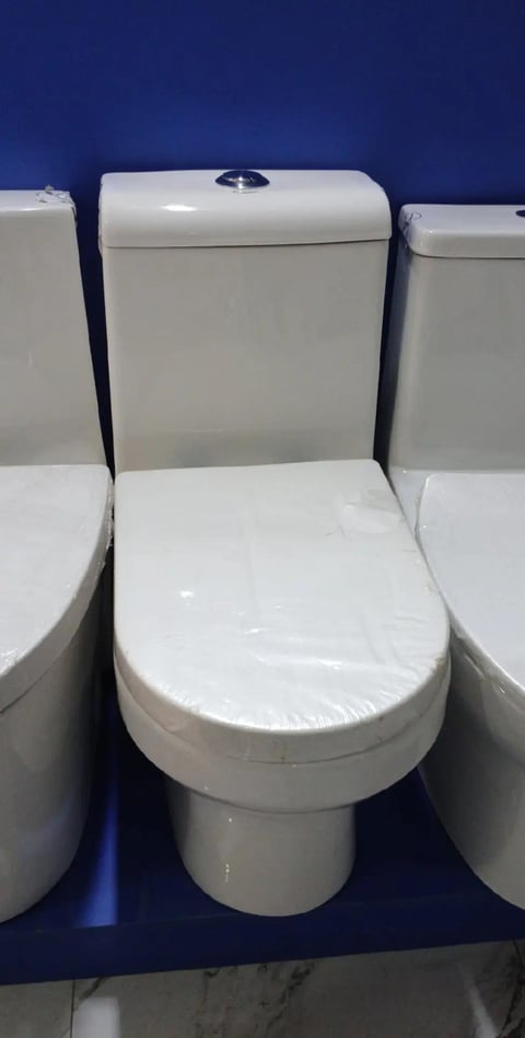 Three white ceramic toilets with closed seats displayed against a dark blue wall in a showroom
