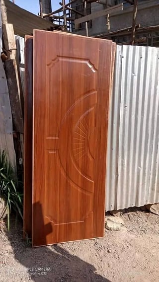 Wooden door with decorative carved panel leaning against corrugated metal fence at construction site