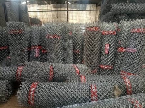 Rolls of galvanized chain-link fencing stacked and bundled with red ties at an outdoor storage facility