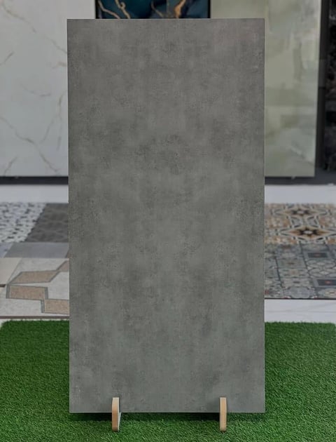 Gray concrete tile sample displayed on green turf with flooring samples in background showroom