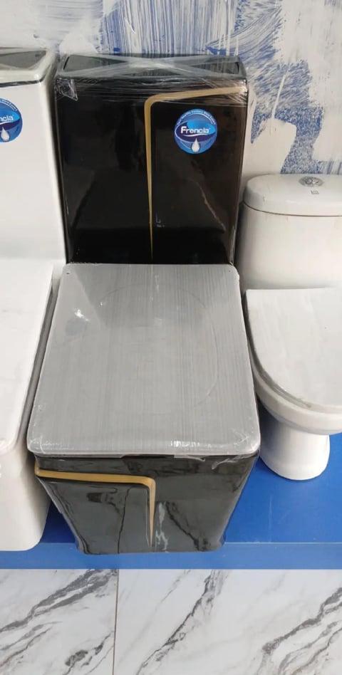 Black toilet with gold trim and white seat on display in showroom with other white toilets and blue tile flooring
