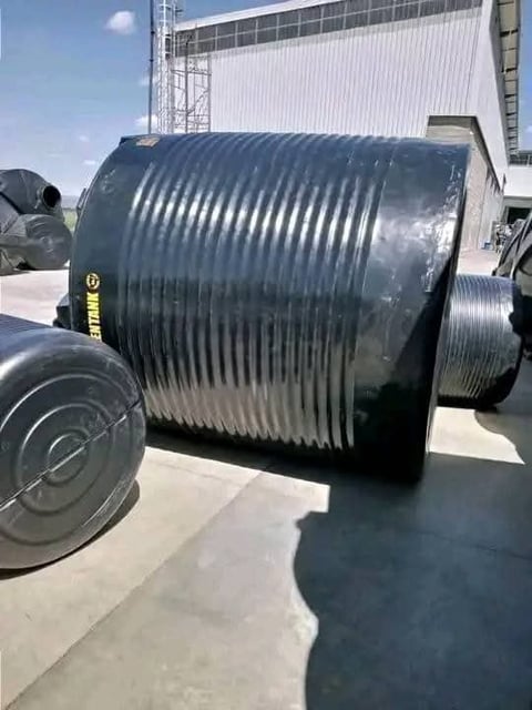 Large metal cylindrical tank with spiral ridges on a truck bed at an industrial facility with white building