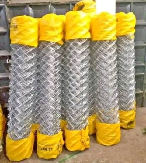 Five rolled galvanized chain-link fencing spools with yellow plastic wrapping on top and bottom