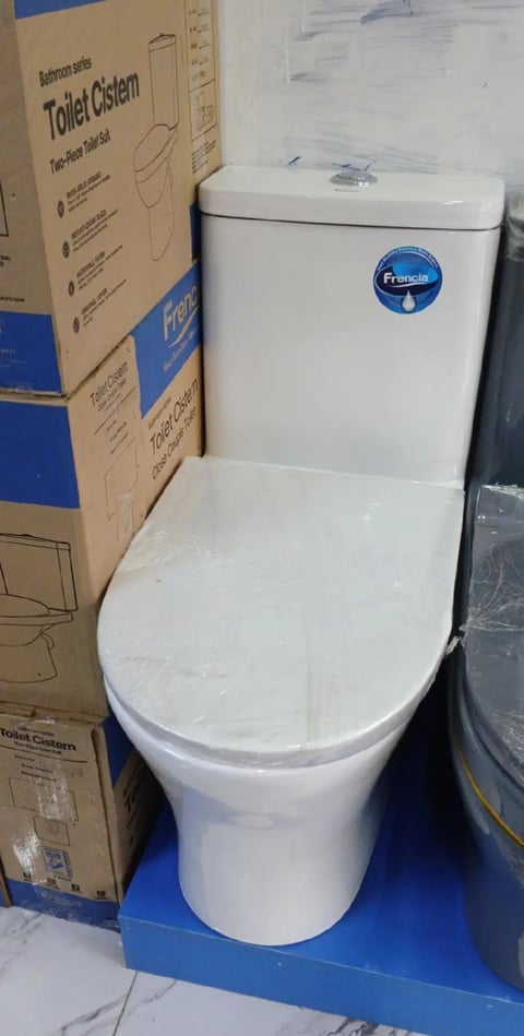White two-piece toilet with blue Francist logo displayed next to cardboard packaging box in showroom setting