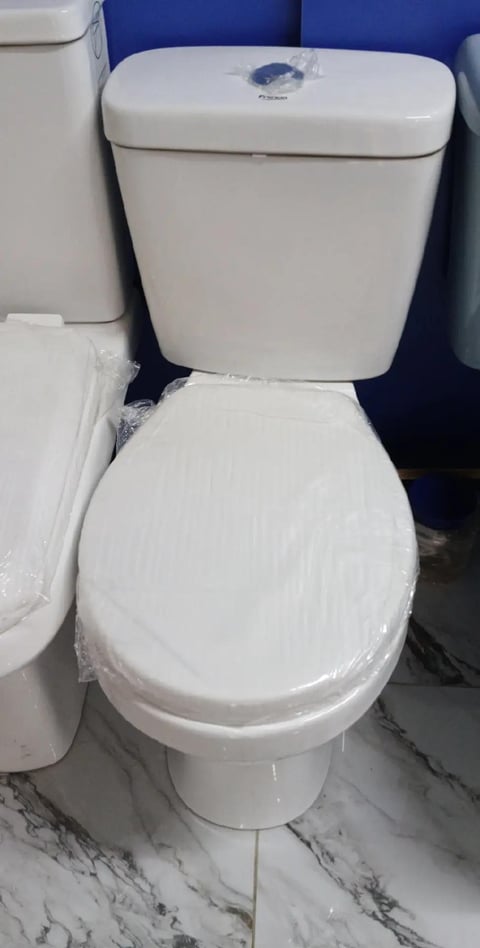 White ceramic toilet with closed lid and plastic wrap, displayed in showroom with blue backdrop