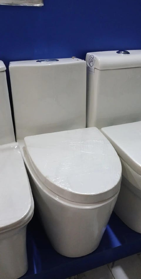 Display of modern white toilet fixtures with closed seats and tanks on a blue wall background in a bathroom showroom