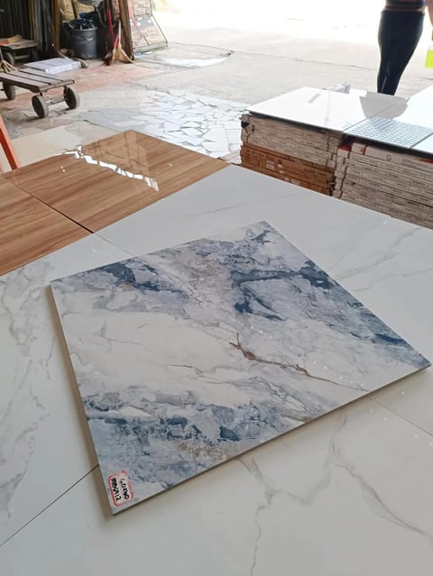 Tile showroom display with white and blue marble-patterned floor tile sample in foreground on white marble surface