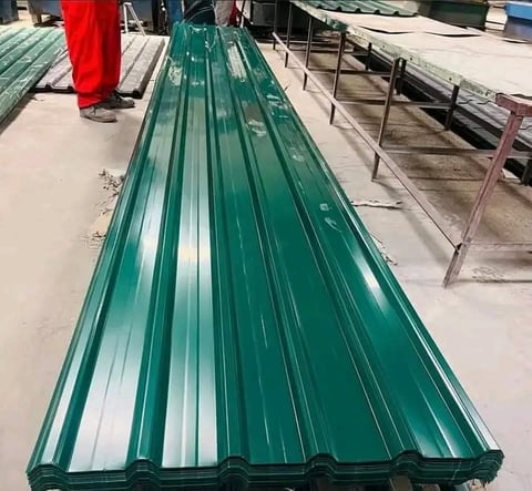 Long green corrugated metal roofing sheet displayed in industrial warehouse with other construction materials