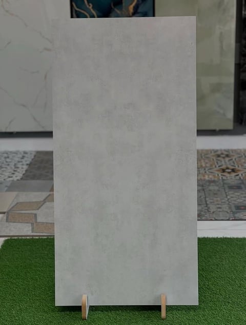 White concrete tile display sample leaning against wooden legs on green turf with flooring samples in background