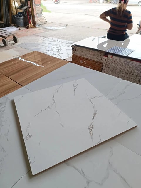 Marble-effect tile and wood flooring samples displayed in a showroom with a woman examining options in the background