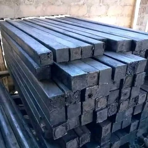 Stack of dark metal square bars and flat stock arranged in rows at an industrial facility