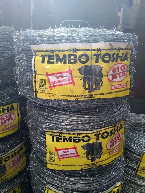 Rolls of barbed wire fencing with yellow Tembo Tosha brand labels wrapped in plastic at a supply warehouse